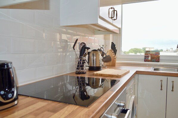 A modern kitchen with a black induction cooktop, wooden cabinets, and a window with a view of the outside.