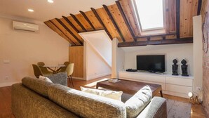 A modern living room with a high ceiling, wooden beams, a TV, and a dining area with chairs. - Charming Flat with A/C & Terrace in Príncipe Real (Lisboa)