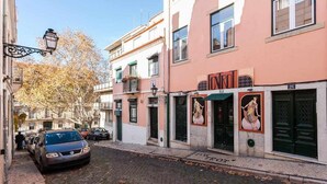 A narrow cobblestone street lined with buildings, including a pink building with a sign that reads "NRO". - Charming Flat with A/C & Terrace in Príncipe Real (Lisboa)