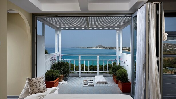 A bedroom with a large bed, a view of the sea, and a balcony with potted plants. - Villa  'Miami' in Villa Paradise Boutique Villas Hotel- Plaka beach (Naxos)
