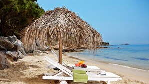 A beach scene with a thatched umbrella, lounge chairs, and a table with fruit and a hat. - Villa  'Miami' in Villa Paradise Boutique Villas Hotel- Plaka beach (Naxos)