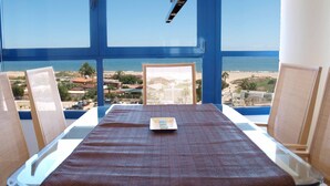 Una habitación con un amplio ventanal con vista a la playa, una mesa con mantel individual y dos sillas.