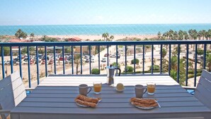Un balcón con una mesa dispuesta para el desayuno, con vista a una playa y al océano.