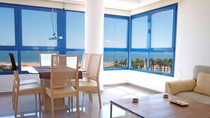 Una sala moderna con vista a la playa, un comedor con sillas y una mesa, y un sofá.