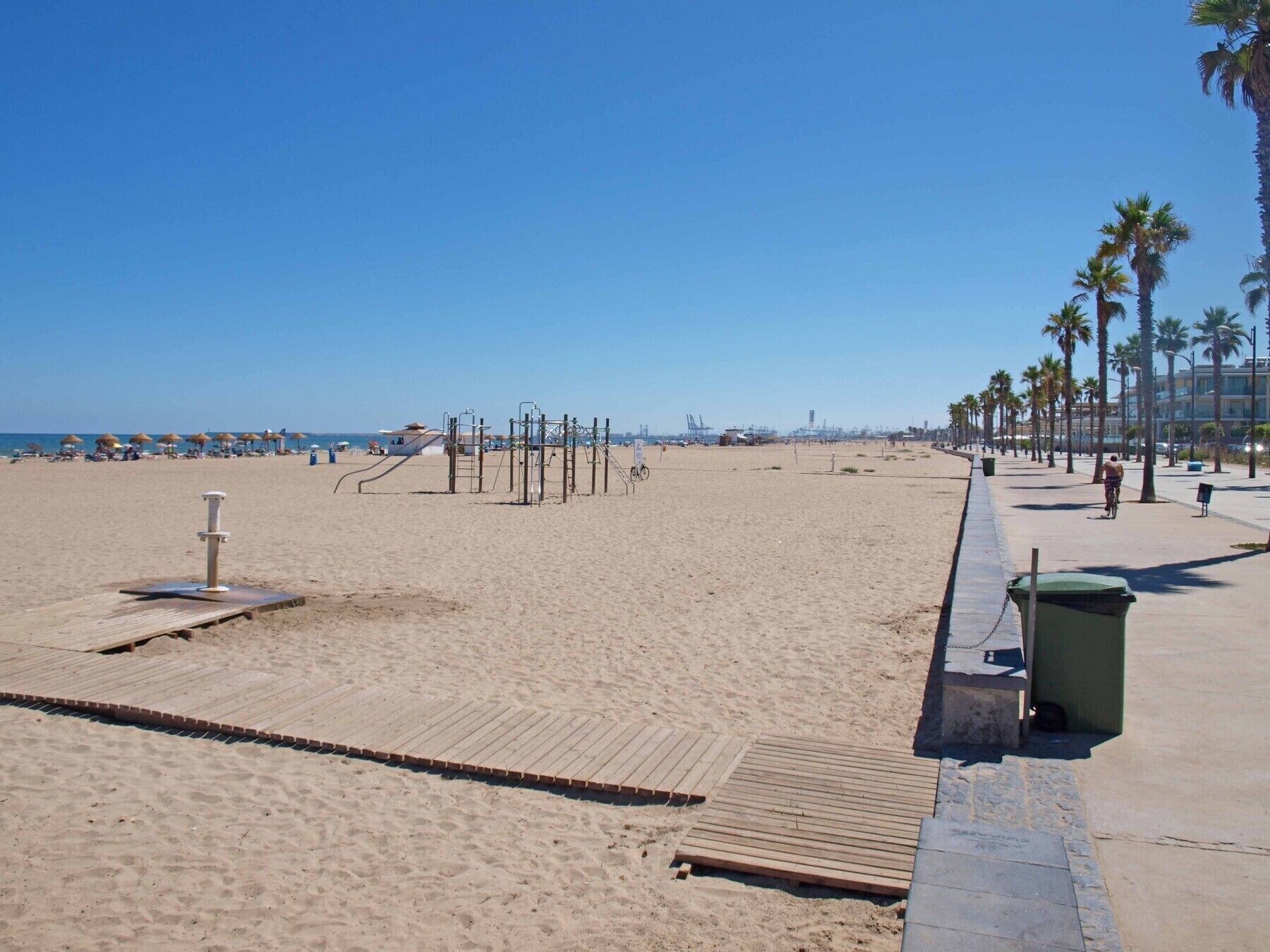 Een strand met houten looppaden, palmbomen en een heldere lucht.