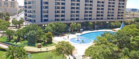Un hotel a più piani con piscina, palme e un prato curato.