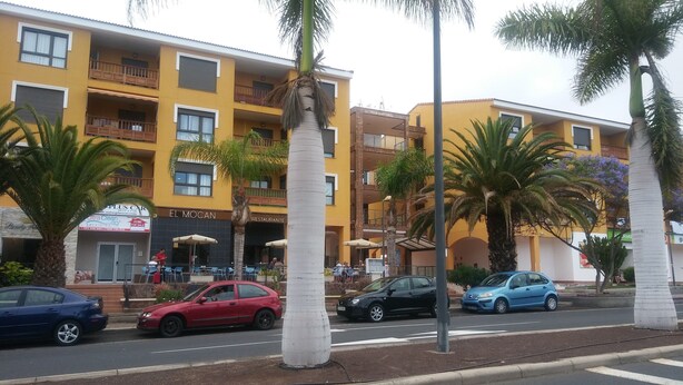 A multi-story yellow building with balconies, a restaurant named 'EL MOCAN', and several parked cars. - COZY APARTMENT IN PALM MAR (arona)