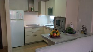 A compact kitchen with a refrigerator, microwave, sink, and a countertop with fruits and a plant. - COZY APARTMENT IN PALM MAR (arona)