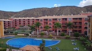 A hotel with a swimming pool, multiple balconies, and a mountainous backdrop. - COZY APARTMENT IN PALM MAR (arona)
