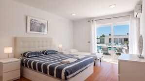 A bedroom with a bed, bedside tables, a framed picture, and a view of a pool and outdoor seating.