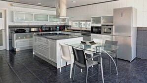 A modern kitchen with a central island, stainless steel appliances, and a glass dining table. - 2 POOLS, FOOTBALL PITCH, TENNIS COURT, CINEMA, GYM, BAR, PRIVATE CHEF, SUNSETS (Poceirão)