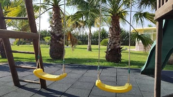 Children can play on the swings and slide in this secure playground area surrounded by lush greenery.