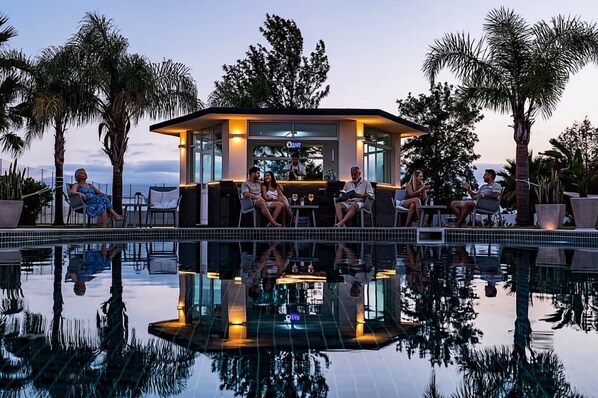 A poolside area with a seating arrangement around a central structure, surrounded by palm trees.