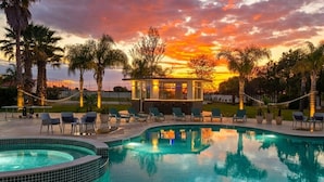 A swimming pool with lounge chairs, palm trees, and a building with a glass facade.