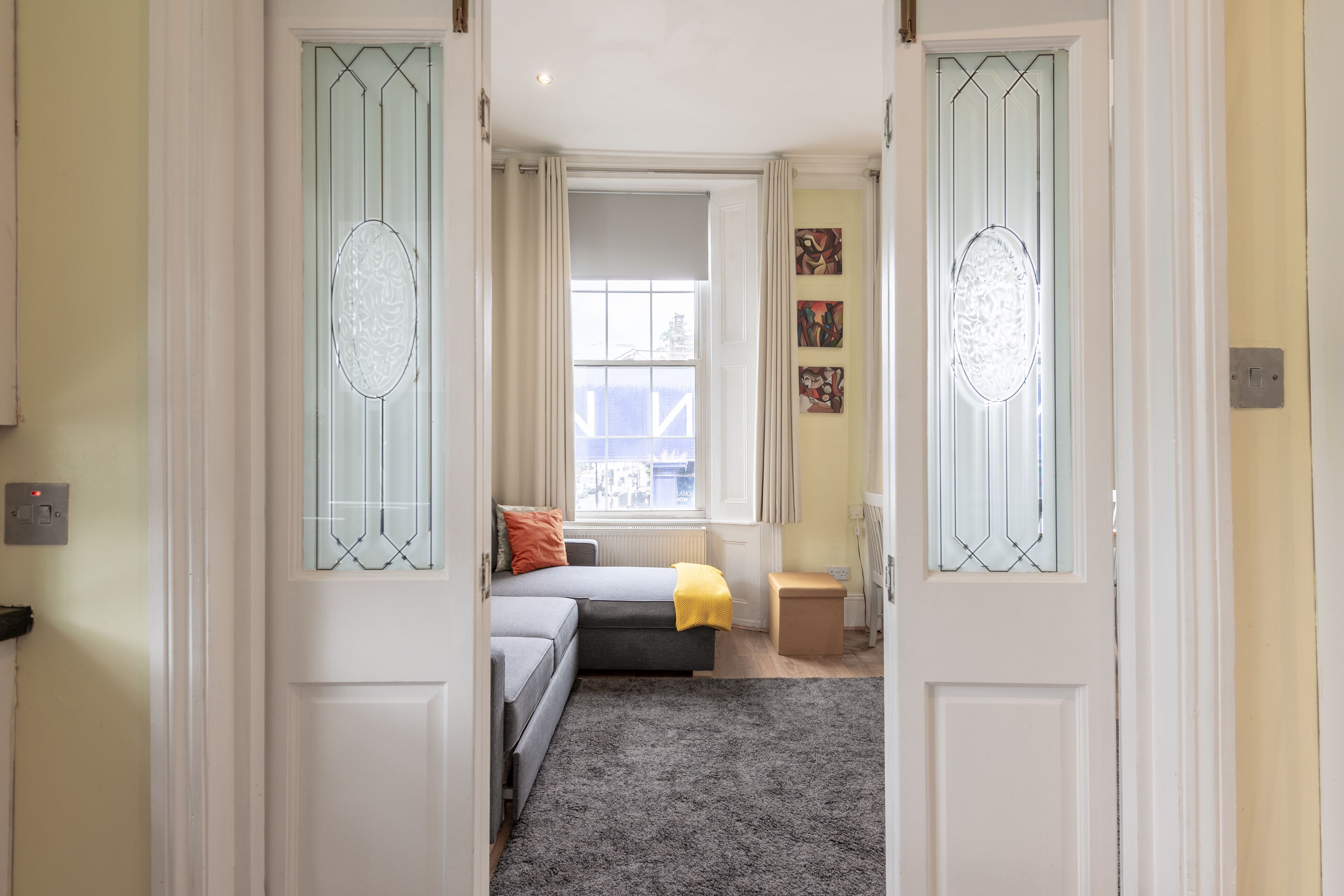 A narrow hallway leading to a bedroom with a bed, a window, and a radiator.