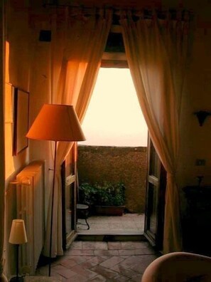 A narrow hallway with a radiator on the left, a lamp, and a view of a balcony with plants. - charming castle apartement with glorious views  (Panzano in Chianti)