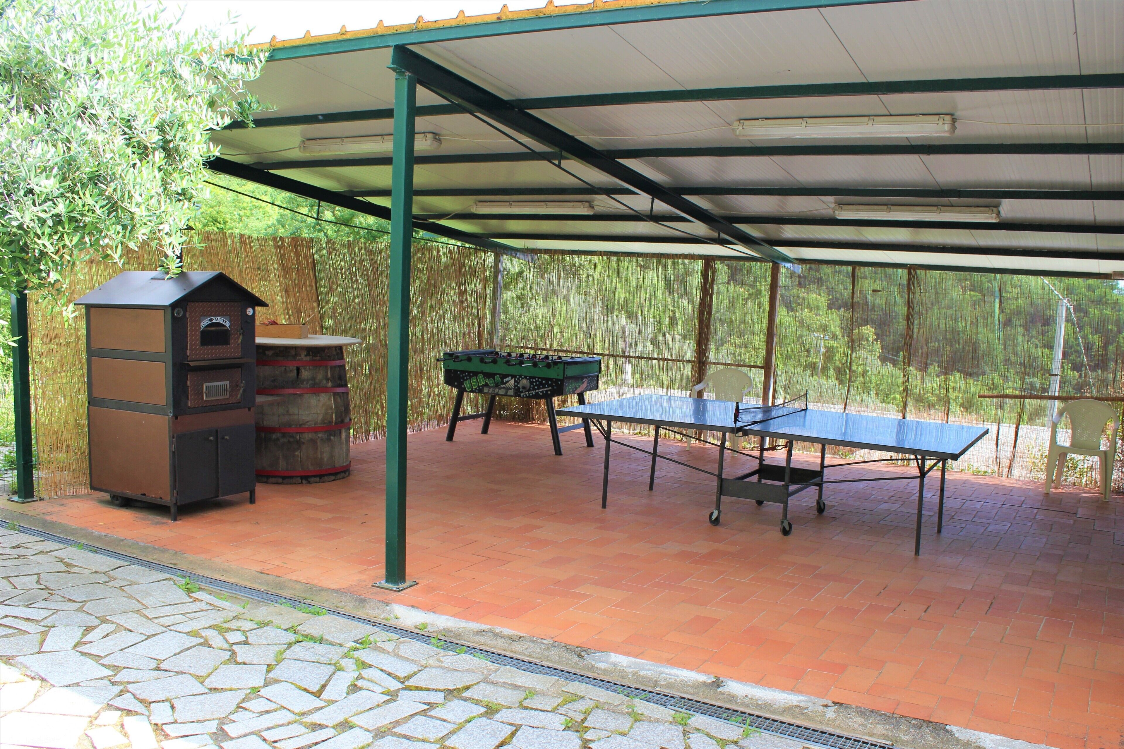 An outdoor patio with a ping pong table, a barbecue grill, and a small oven.