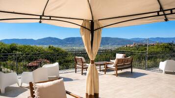 Una terrazza con mobili da esterno, un ombrellone grande e una vista panoramica sulle montagne.
