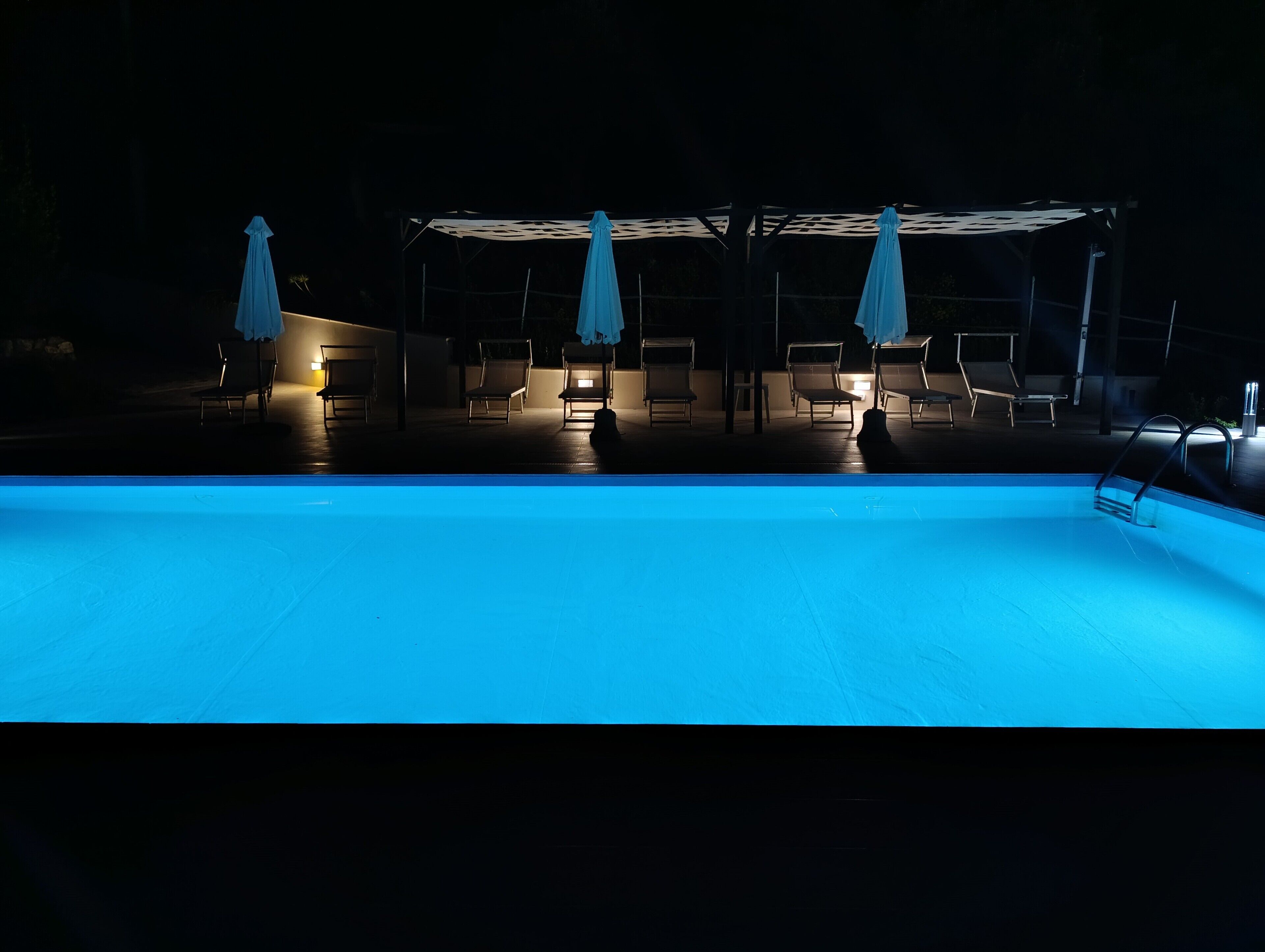 Una piscina con sillas de descanso y sombrillas bajo una zona cubierta.