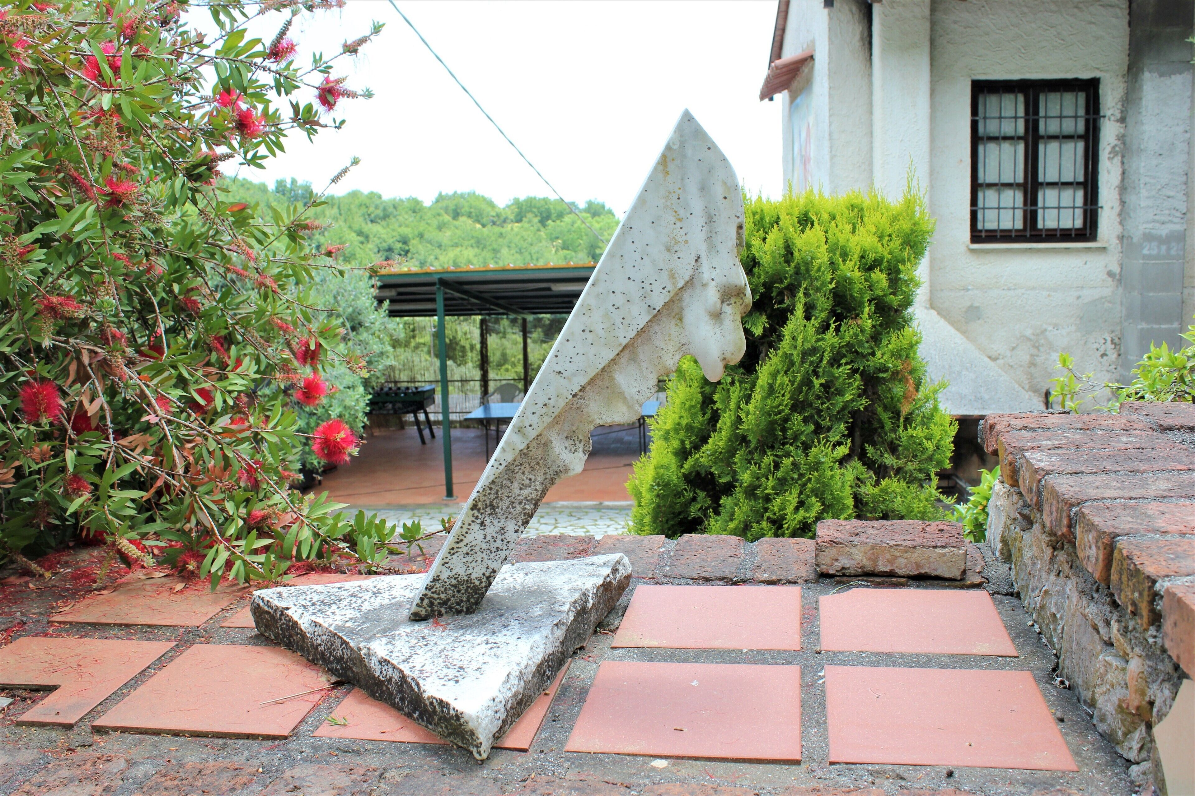 Eine Steinskulptur in einem Garten mit roten Ziegeln und grünen Büschen.