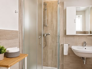 Un bagno moderno con cabina doccia in vetro, un mobile bagno in legno con lavello e uno specchio sopra il lavello.