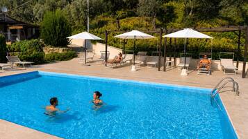 Piscina con sillas de descanso y sombrillas, rodeada de follaje.