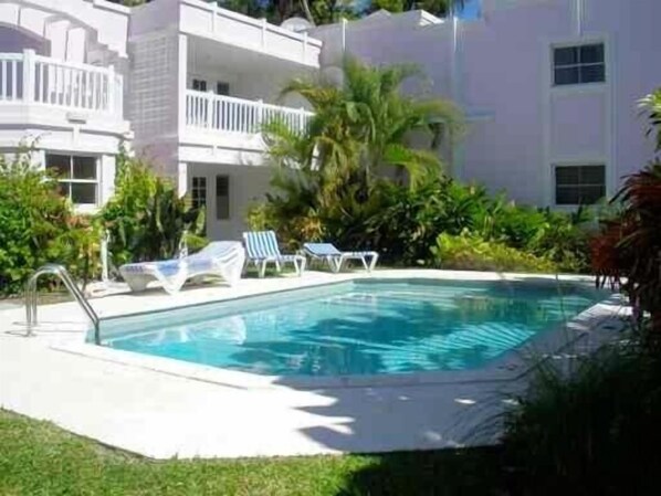 Un área de piscina con sillones reclinables y un edificio con balcones.