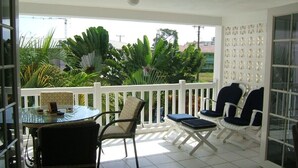 A balcony with a glass table, chairs, and a white railing.