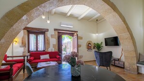 A spacious living room with a round table, red sofa, and a stone archway. - Private Pool★Stone Villa★ BBQ & Wifi★ Jacuzzi (Astratigos)