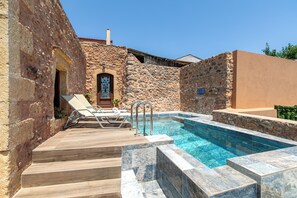 Un espace piscine entouré de murs en pierre, avec des marches menant à une porte, et bordé d’une terrasse en bois.