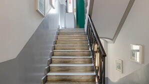 A marble staircase with a black railing leading to a green door at the top.