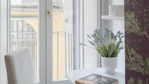 A room with a white chair, a small table with a book and a potted plant, and a white door leading to an outdoor balcony.