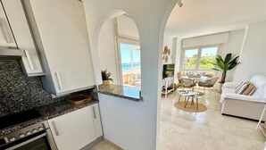 A modern kitchen with a built-in oven, a dining area with a round table, and a living room with a sofa. - Sunrise 01 by homeprive (Denia)