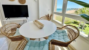 A room with a round table, wicker chairs, a flat-screen TV, and large windows with a beach view. - Sunrise 01 by homeprive (Denia)