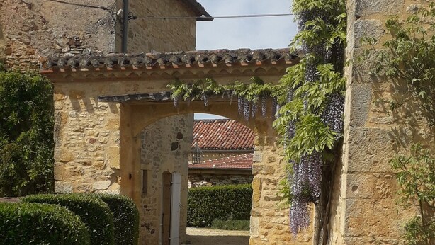 A courtyard with stone walls, a gravel path, and a building with a tiled roof.