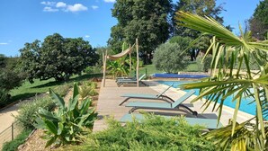 A pool area with lounge chairs, a wooden deck, and tropical plants.