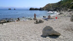 Een kiezelstrand met mensen die zwemmen en zonnebaden, een rode emmer en een gestreepte parasol.
