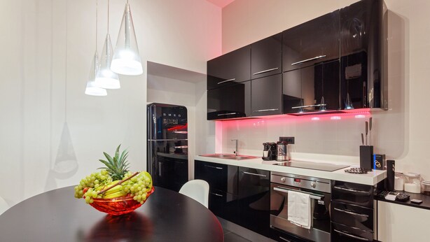 A modern kitchen with black cabinets, stainless steel appliances, and a red bowl of fruit on the table. - New duplex apts in VATICAN - M + I (Roma)