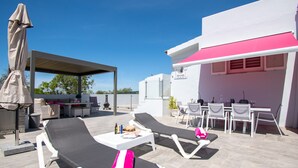 En tagterrasse med liggestole, et spiseområde og et overdækket siddeområde.
