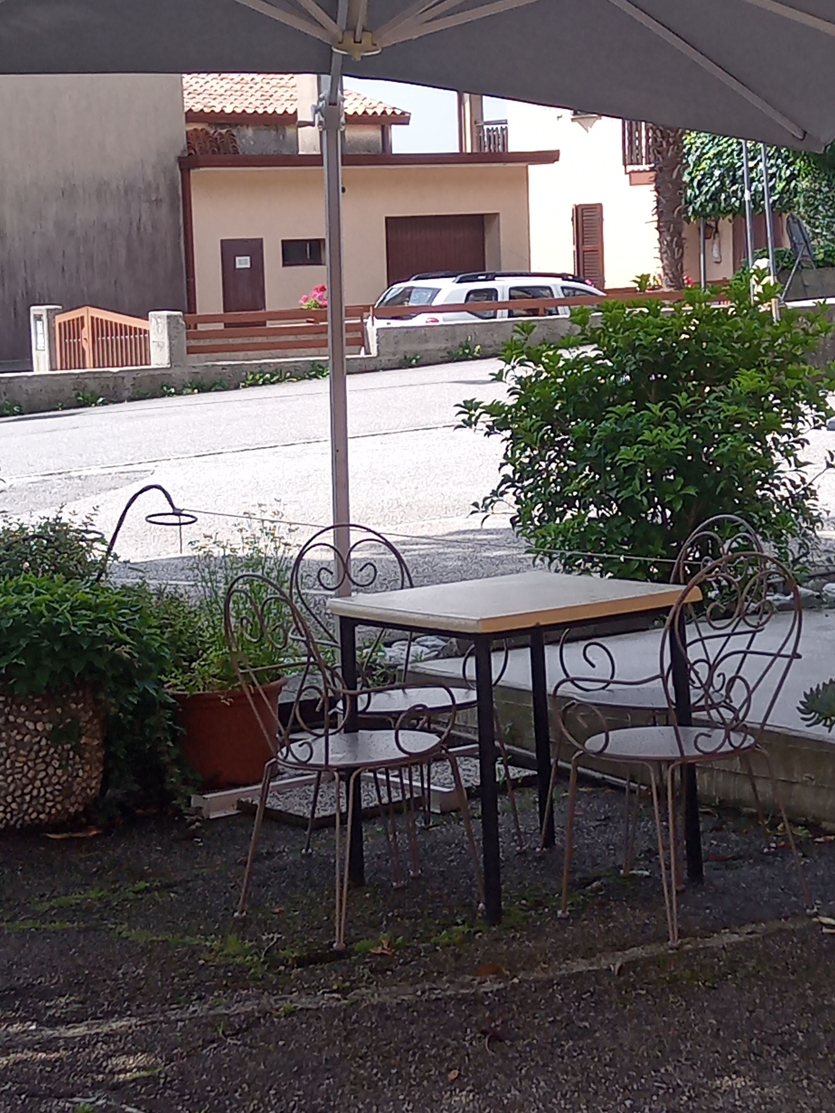 Ein Außenbereich mit Tisch und Stühlen, einer Topfpflanze und Blick auf eine Straße mit Gebäuden und parkenden Autos.