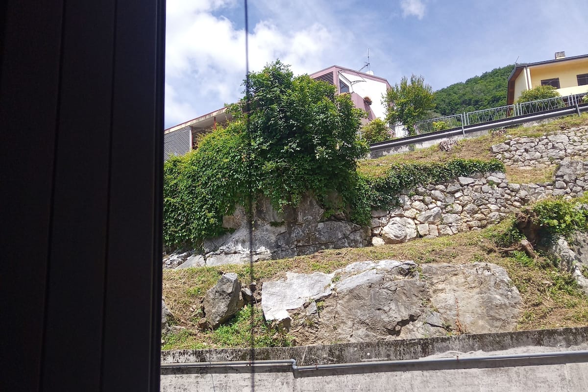 A view through a window with a concrete wall, a stone wall, and a metal railing.