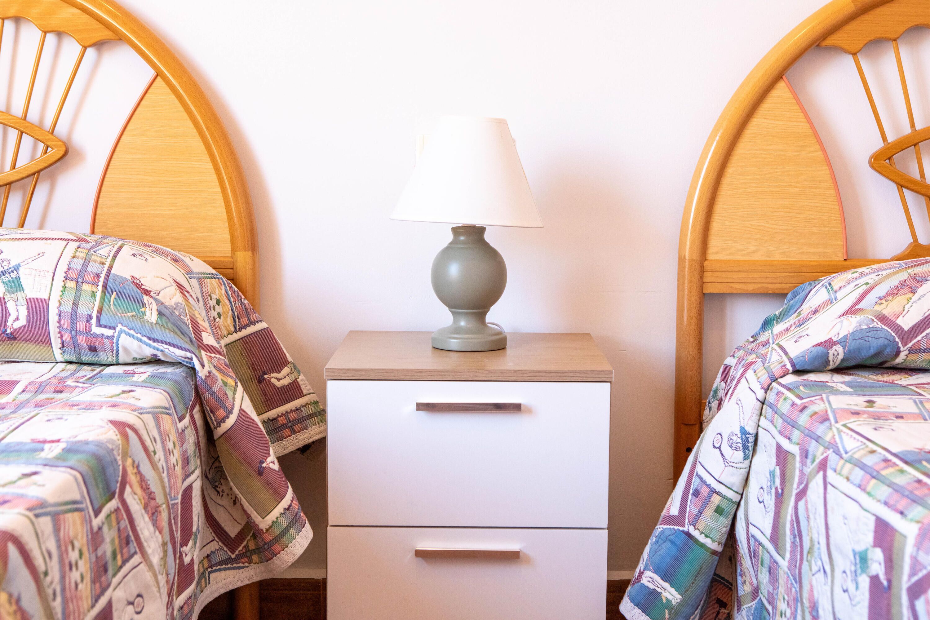 Een kamer met twee houten bedden, elk voorzien van beddengoed met een patroon, een nachtkastje met een lamp en een lade.