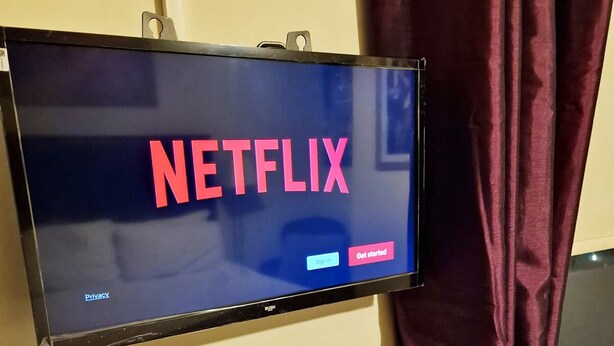 A flat-screen TV mounted on a wall displaying the Netflix logo with options to sign in and get started. - Stay Norwich Apartments Trade Stay House (Norfolk)