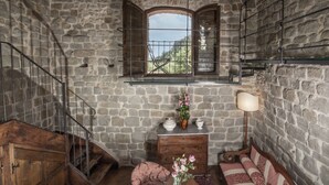 Ein rustikaler Raum mit Steinwand, einer Holztreppe, einem Fenster mit Aussicht, einer hölzernen Bank und einem Schrank mit Blumenvase.