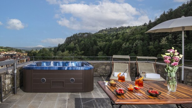 Ein Whirlpool auf einer Terrasse mit einem Tisch, der für eine Mahlzeit gedeckt ist, umgeben von einer malerischen Aussicht auf Hügel und Bäume.