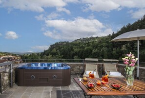 Ein Whirlpool auf einer Terrasse mit einem Tisch, der für eine Mahlzeit gedeckt ist, umgeben von einer malerischen Aussicht auf Hügel und Bäume.