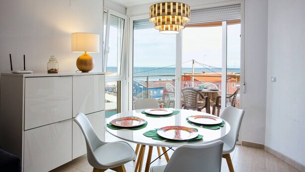 Un coin repas avec une table dressée pour quatre personnes, une lampe et une vue sur la mer.