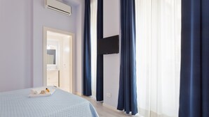 Een slaapkamer met een bed, een flatscreen televisie aan de muur en een raam met gordijnen.