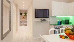 Een moderne keuken met witte kasten, een flatscreen televisie en een fruitschaal op het aanrecht.