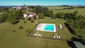 Vue aérienne d’une propriété dotée d’une piscine, de chaises longues et d’une grande maison entourée de verdure.